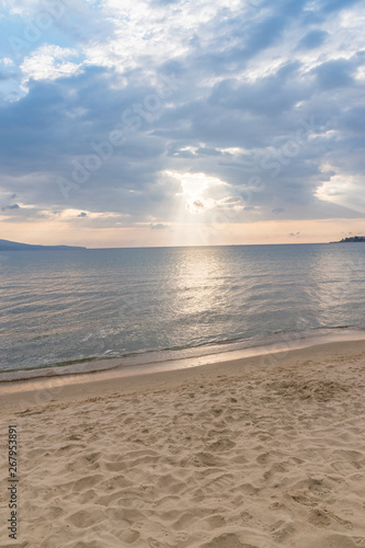 Sunbeams or sun rays peeking through the clouds at a sunrise on beautiful beach