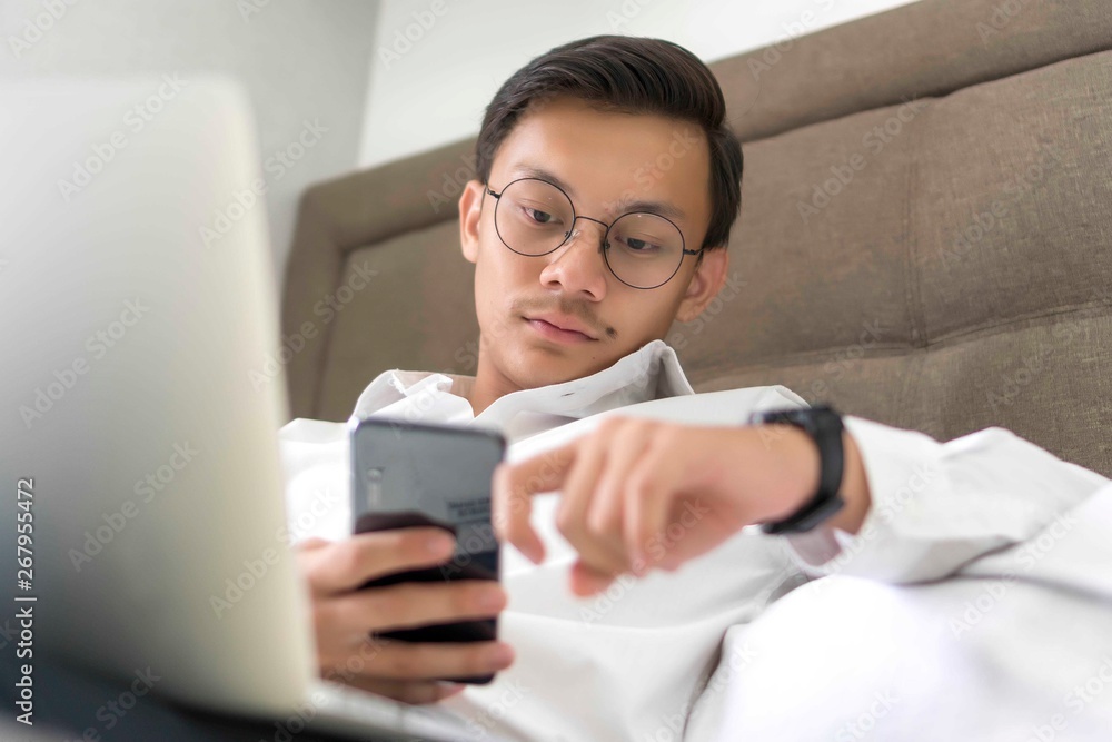 Young Malay Muslim working with laptop at the bed looking at the phone Young Malay Muslim working with laptop at the bed looking at the phone