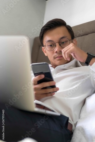 Young Malay Muslim working with laptop at the bed looking at the phone