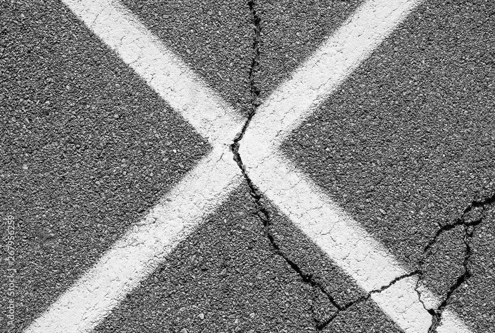 Abstract urban white x with crack. Asphalt blacktop with white painted x.