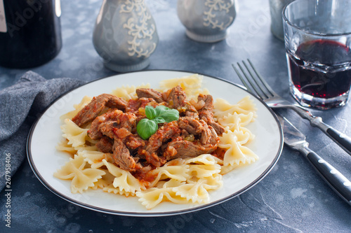 Beef in tomato sauce with farfalle on a white plate, horizontal