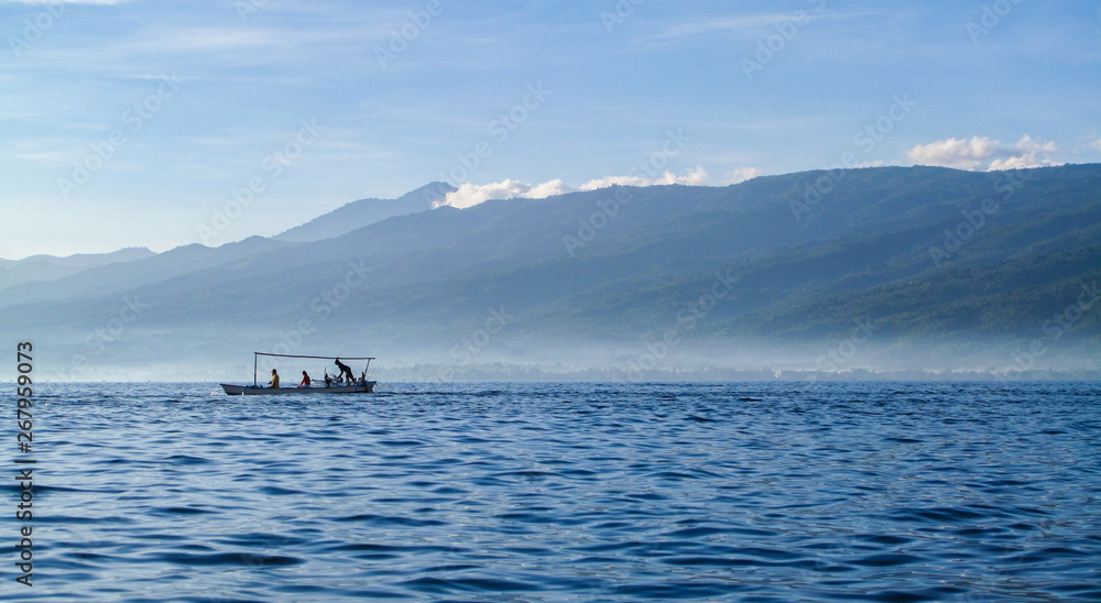 Small local boat sailing in an open sea with range of mountains in the background.