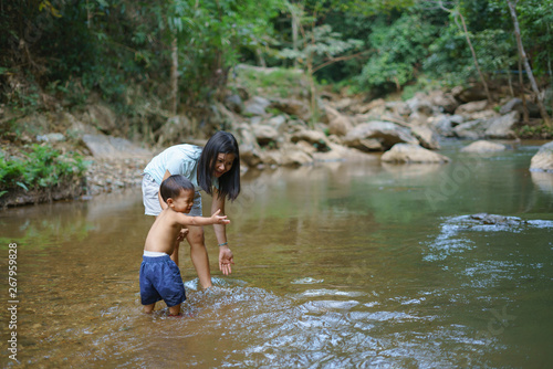 Fototapeta Naklejka Na Ścianę i Meble -  Asian mother in blue shirt with DIY chest pocket playing water with her son about 1 year and 9 months at  waterfall