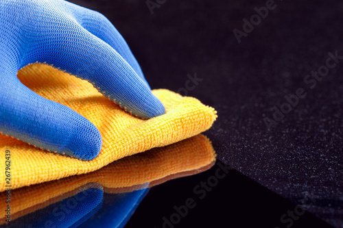 Employee hand in protective glove wiping dust layers on the furniture  with yellow dry rag. photo