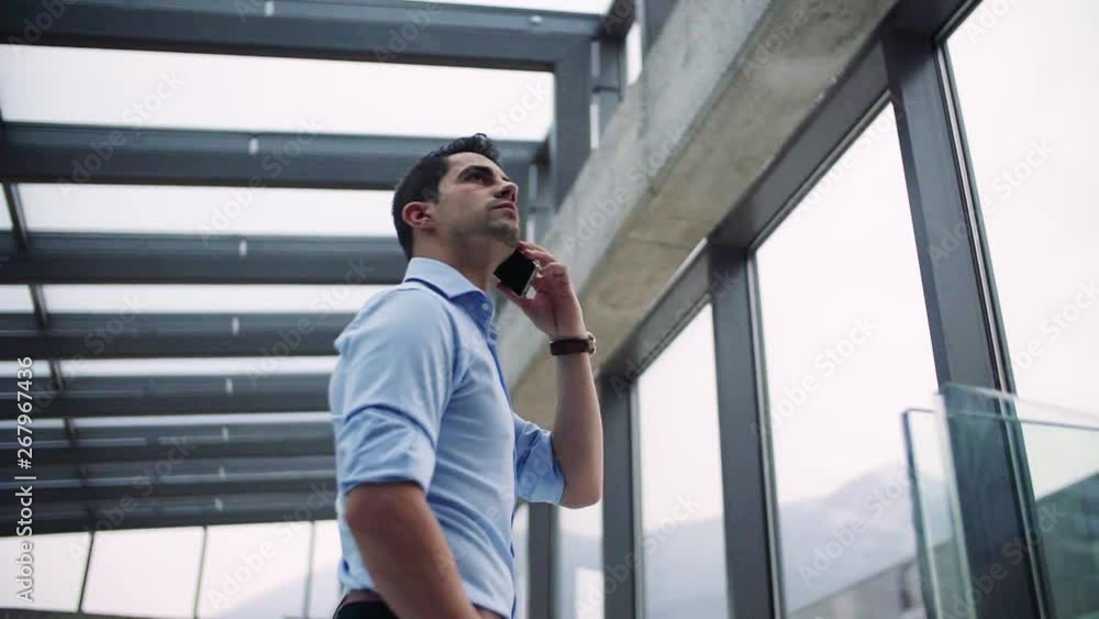 A young businessman with smartphone in corridor outside office. A young businessman with smartphone in corridor outside office.