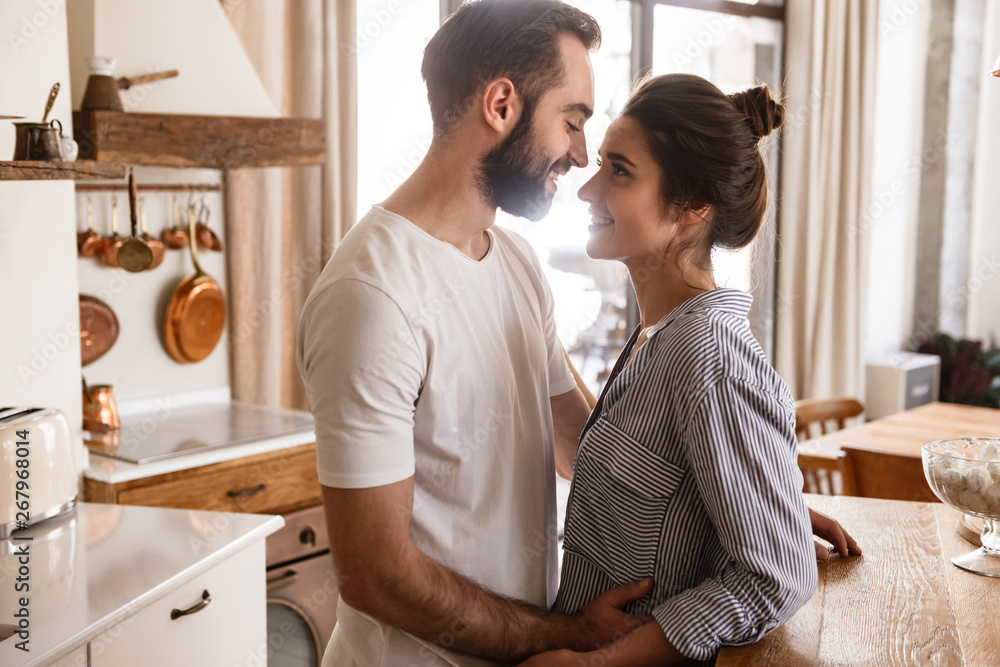 Image of adorable brunette couple in love smiling while hugging together in apartment Image of adorable brunette couple in love smiling while hugging together in apartment
