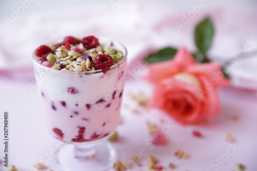 yogurt parfait with fresh raspberry berries and rose on a light pink background. Healthy food. With copy space for text.