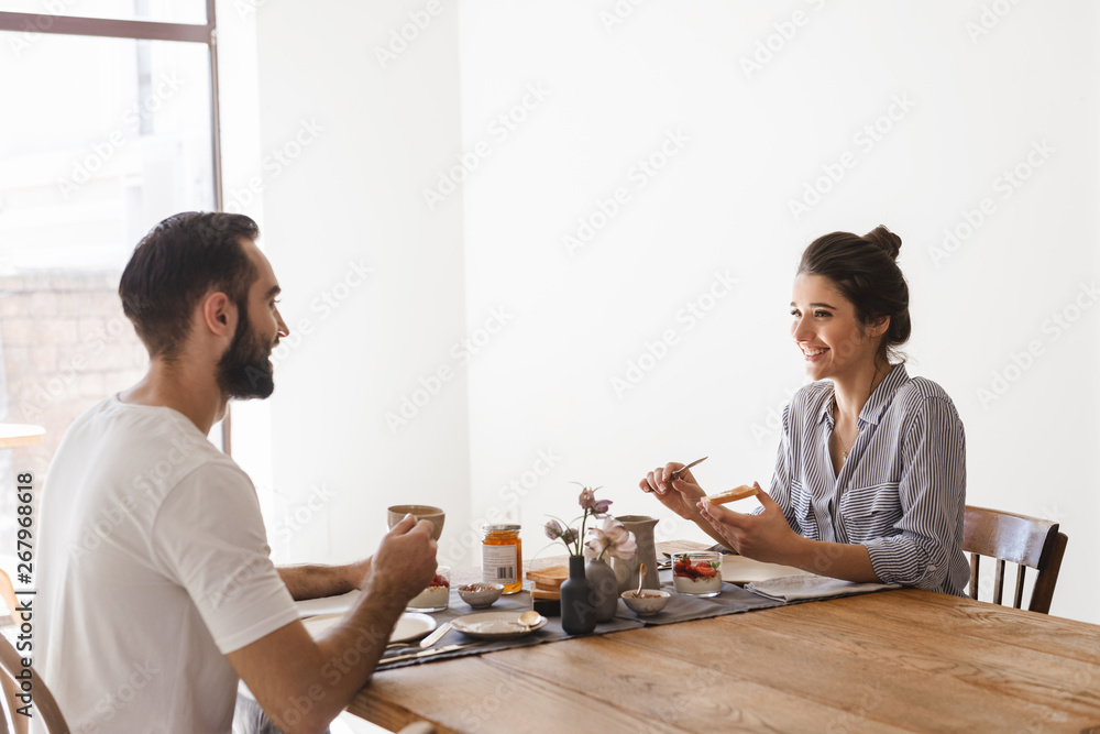 Image of caucasian brunette couple eating together at table while having breakfast in apartment Image of caucasian brunette couple eating together at table while having breakfast in apartment