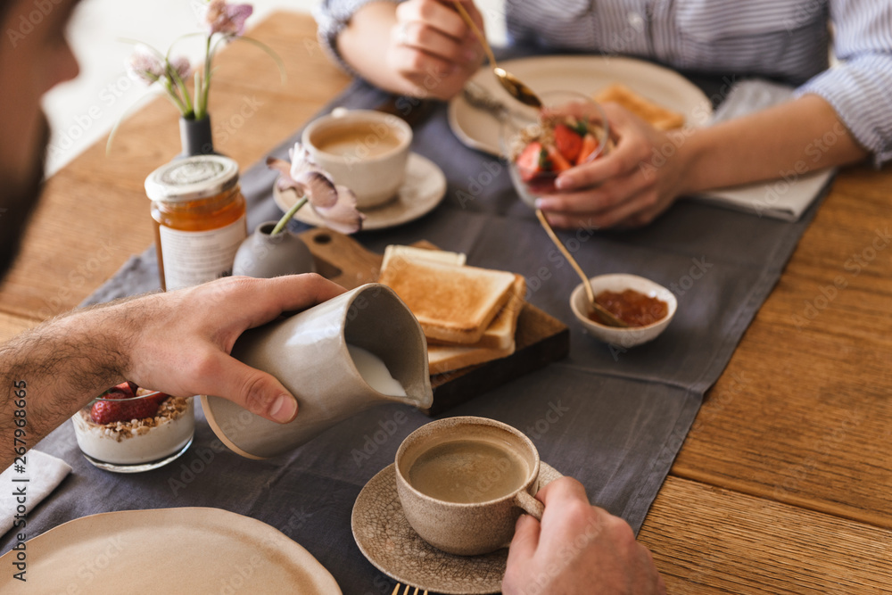© Drobot Dean - Image of modern happy couple eating together at table while having breakfast in apartment © Drobot Dean - Image of modern happy couple eating together at table while having breakfast in apartment