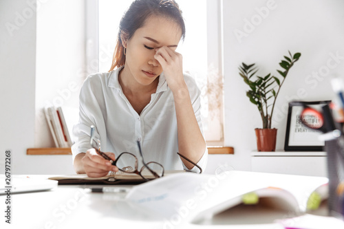 Tired asian business woman sitting by table with closed eyes