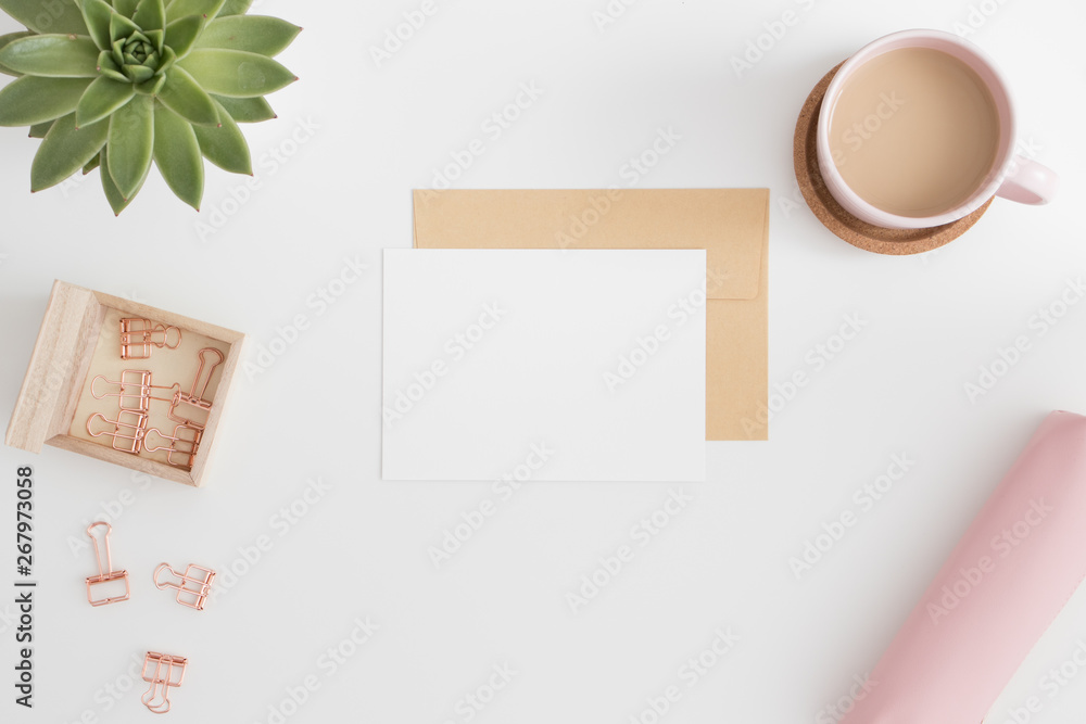 Top view of a white card mockup and envelope with workspace accessories on a white table. Top view of a white card mockup and envelope with workspace accessories on a white table.