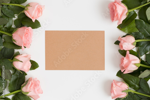 Top view of a kraft card mockup with pink roses on a white table.