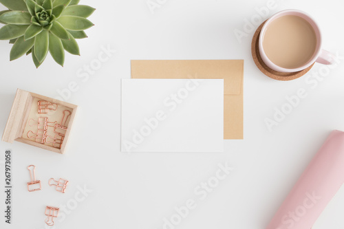 Top view of a white card mockup and envelope with workspace accessories on a white table.