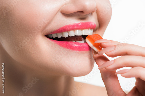 Fototapeta Naklejka Na Ścianę i Meble -  cropped view of smiling young woman eating orange jelly candy isolated on white