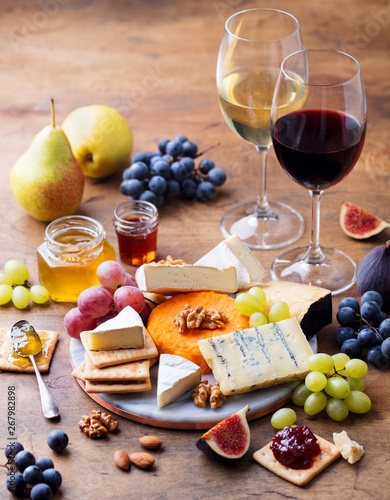Grape, cheese, figs and honey with a glasses of red and white wine on a wooden background.