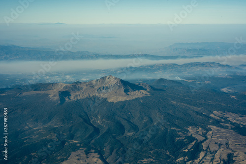 old volcano surrounded by forrest in mexico in flight with clouds and blue sky