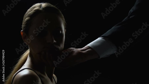 Cruel man looking at beautiful face of young woman on black background, trade