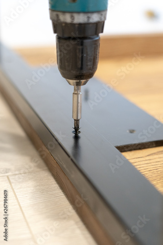Man using screwdriver fasten metal element on wooden table top