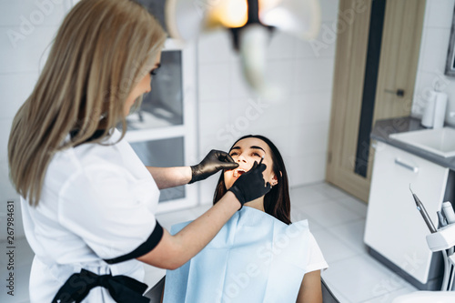 Pretty young female dentist making examination and treatment for young female patient in dental clinic.