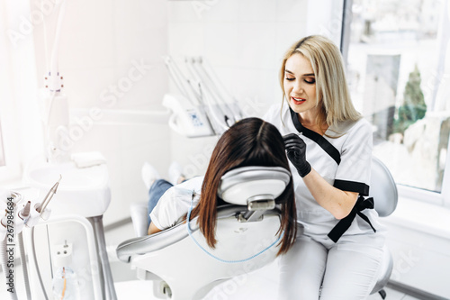 Pretty young female dentist making examination and treatment for young female patient in dental clinic.