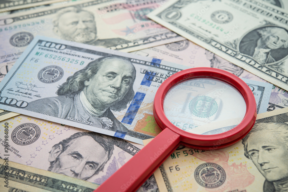 Red magnifying glass on US dollars paper banknote bill background. Concept of find out refinance, bank deposit money saving with high interest, the best investment for high profit growth, stock, bond. Red magnifying glass on US dollars paper banknote bill background. Concept of find out refinance, bank deposit money saving with high interest, the best investment for high profit growth, stock, bond.
