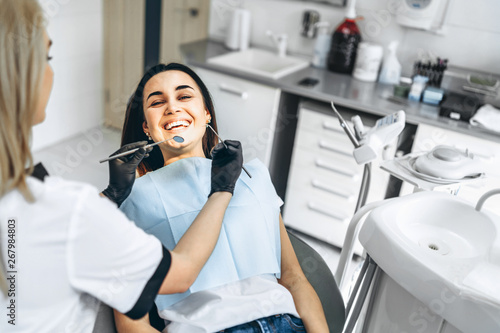Pretty young female dentist making examination and treatment for young female patient in dental clinic.