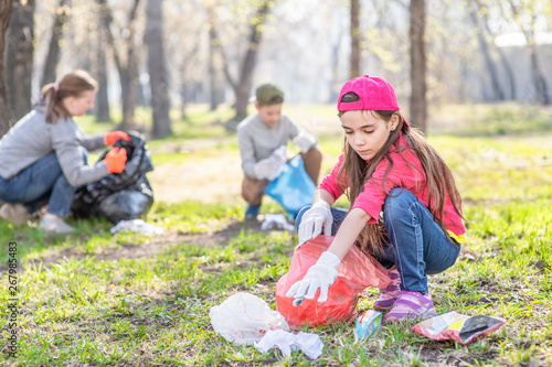 Young girl picking up trash in the park. Volunteer concept photo