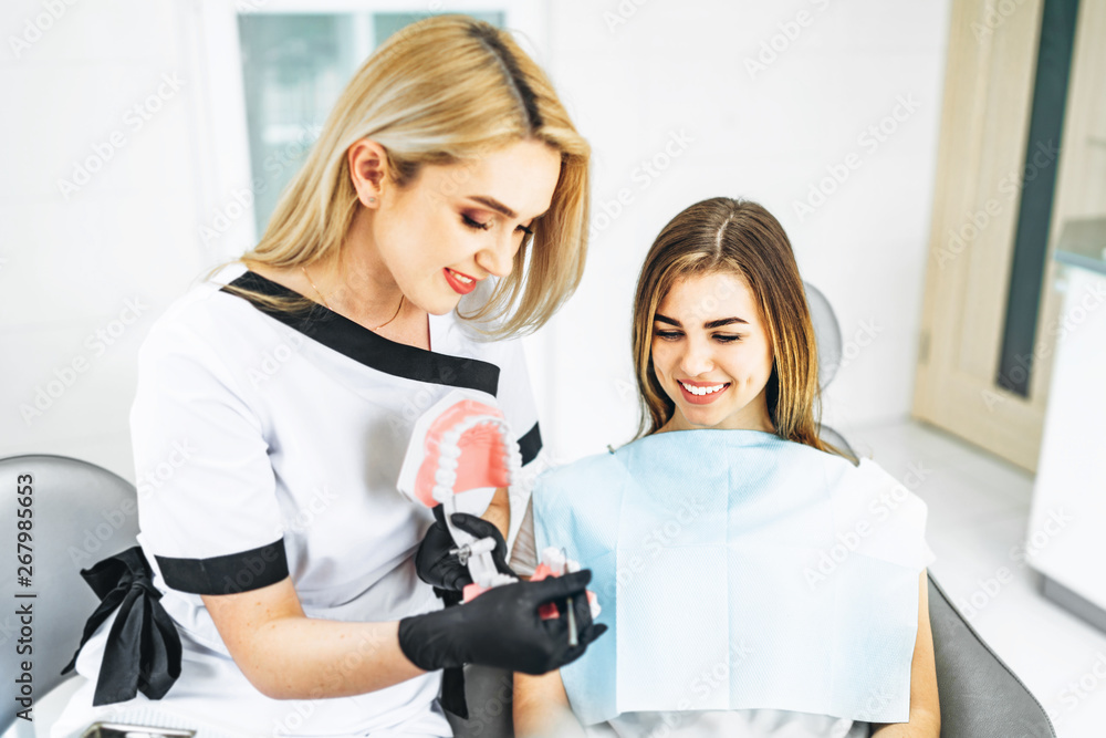 Pretty female dentist explaining way of treatment on the denture for the patient in the clinic. Pretty female dentist explaining way of treatment on the denture for the patient in the clinic.