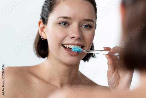 cheerful young woman brushing teeth in front of mirror