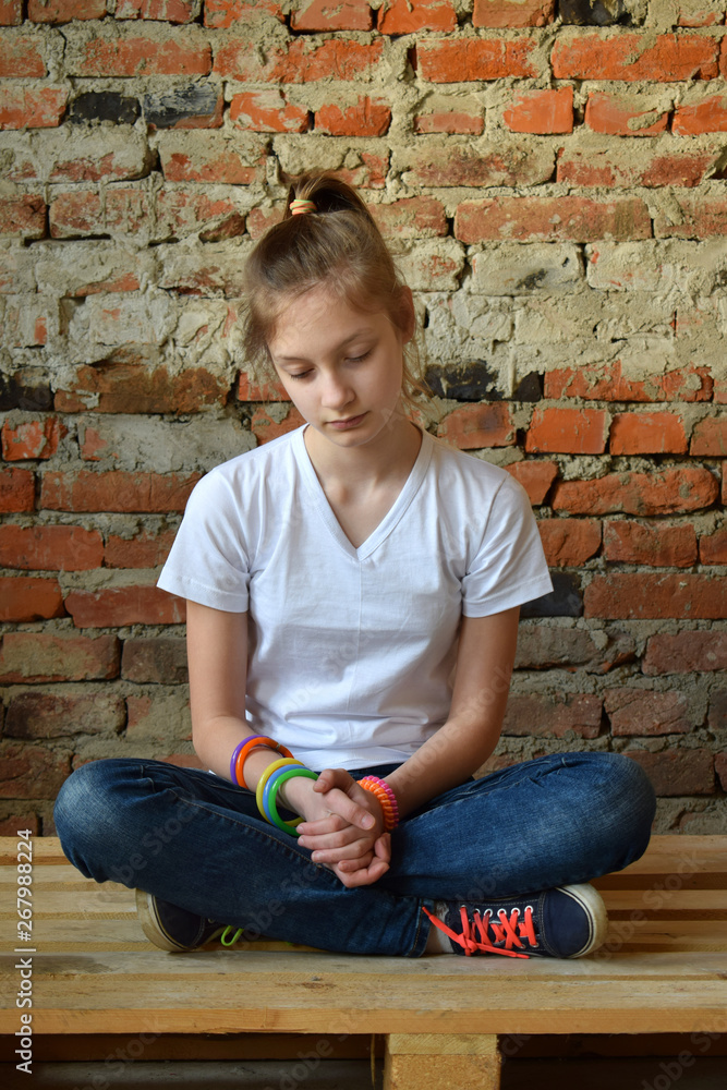 Young girl in jeans and white T-shirt is sitting on the floor and sad. Concept of a non happy teenager. Young girl in jeans and white T-shirt is sitting on the floor and sad. Concept of a non happy teenager.