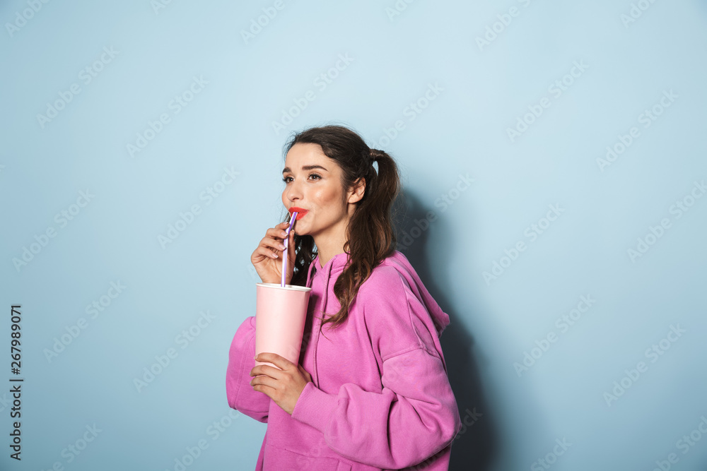 Portrait of joyful young woman with two ponytails smiling while drinking soda beverage from plastic cup Portrait of joyful young woman with two ponytails smiling while drinking soda beverage from plastic cup
