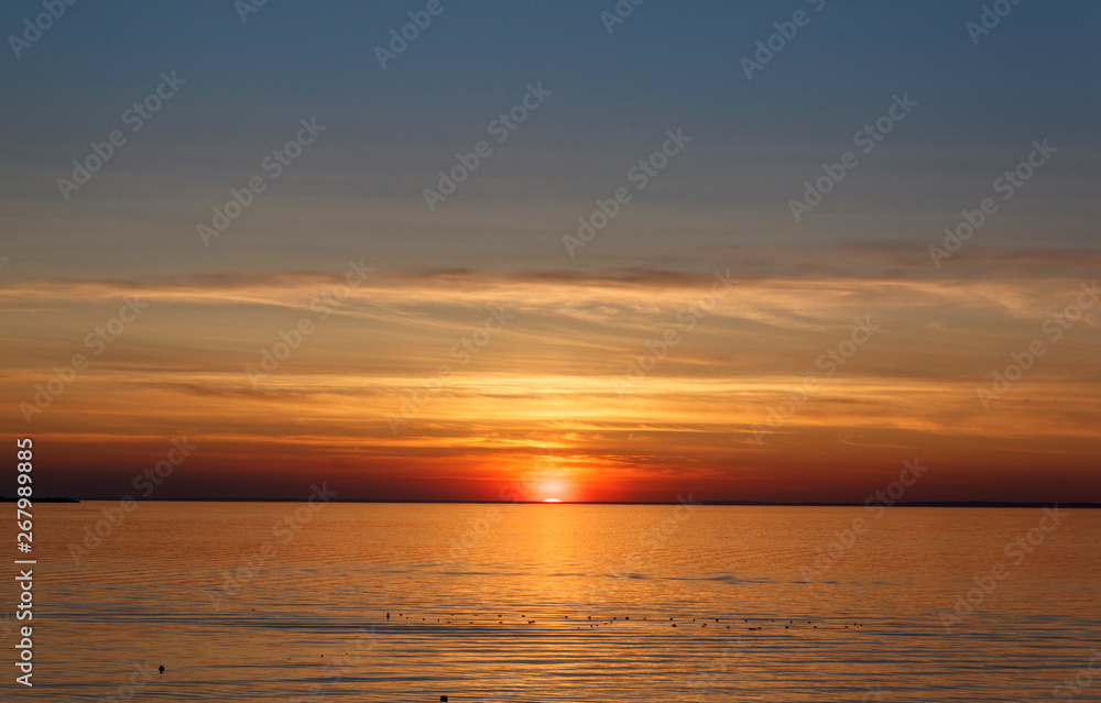 Beautiful sunset over the sea. The sun sets on the water. The sky is painted with bright colors. Sunset beach in a summer evening. Gulf of Finland, Baltic sea, Kronstadt, Saint-Petersburg, Russia.
