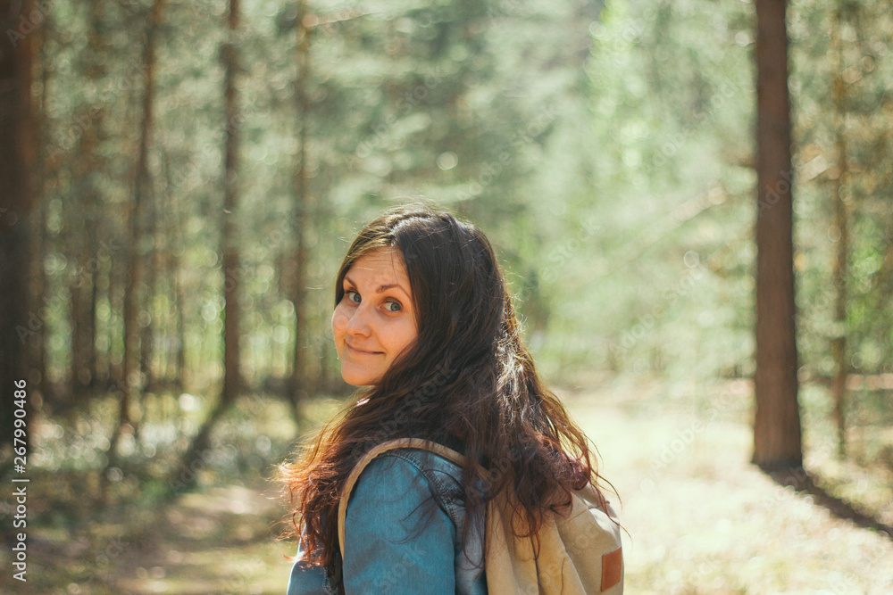 brunette woman with backpack and denim jacket stands in the woods,selective focus brunette woman with backpack and denim jacket stands in the woods,selective focus
