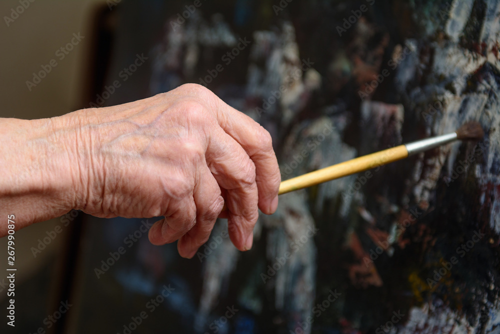 In the hand of an elderly woman artistic brush, which she paints a picture