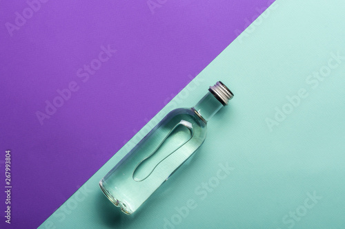 transparent wineglass and bottle with water on bright purple and azure background 