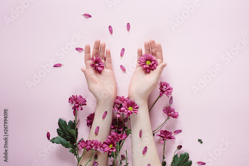 Creative composition. Beautiful female hand with purpure flowers on pink background. Cosmetics for hands anti wrinkle.Top view, copy space