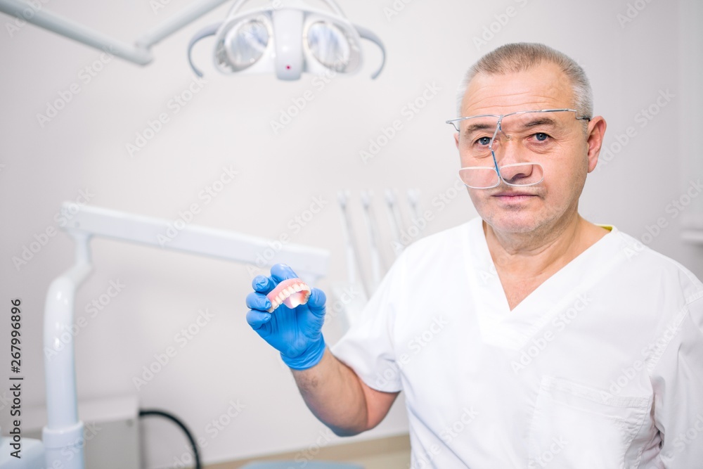 Adult dentist holding a denture in front of him / her in a dental clinic Adult dentist holding a denture in front of him / her in a dental clinic
