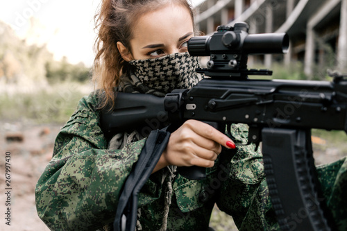 Canvastavla Armed woman in camouflage holding a sniper rifle aims at the target close-up