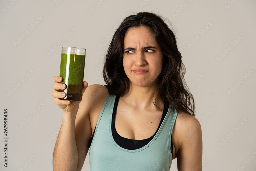 Beautiful young sports latin woman boring of diet holding green smoothie in dislike Beautiful young sports latin woman boring of diet holding green smoothie in dislike