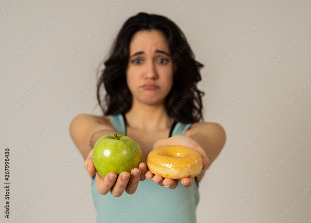 Attractive young woman on a diet deciding between an apple and a doughnut Attractive young woman on a diet deciding between an apple and a doughnut