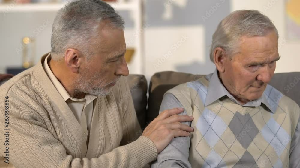 Aged male comforting sad friend sitting on sofa, nursing home, loss support Aged male comforting sad friend sitting on sofa, nursing home, loss support