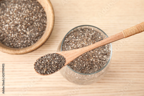 Glass of water with chia seeds and spoon on wooden background, top view
