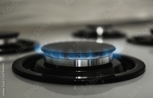 Gas burner with blue flame on modern stove, closeup