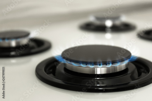 Gas burner with blue flame on modern stove, closeup