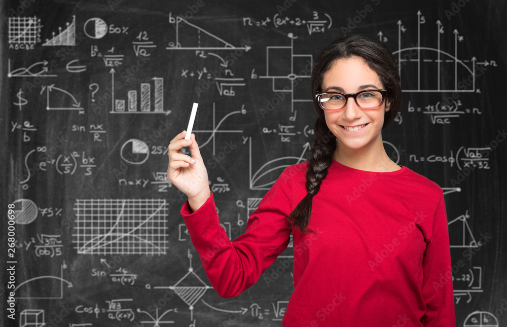 Young teenager holding a chalk and resolving complex formulas on a blackboard