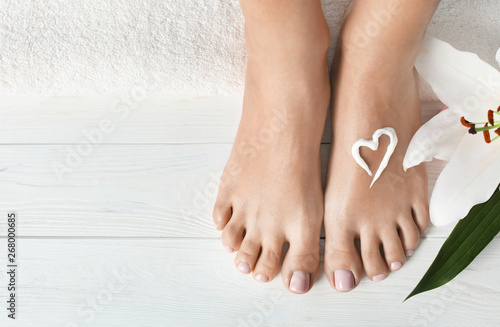 Fototapeta Naklejka Na Ścianę i Meble -  Woman with beautiful feet, cream, flower and towel on white wooden floor, closeup. Spa treatment