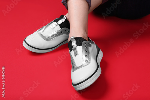 Woman in stylish shoes sitting on color background