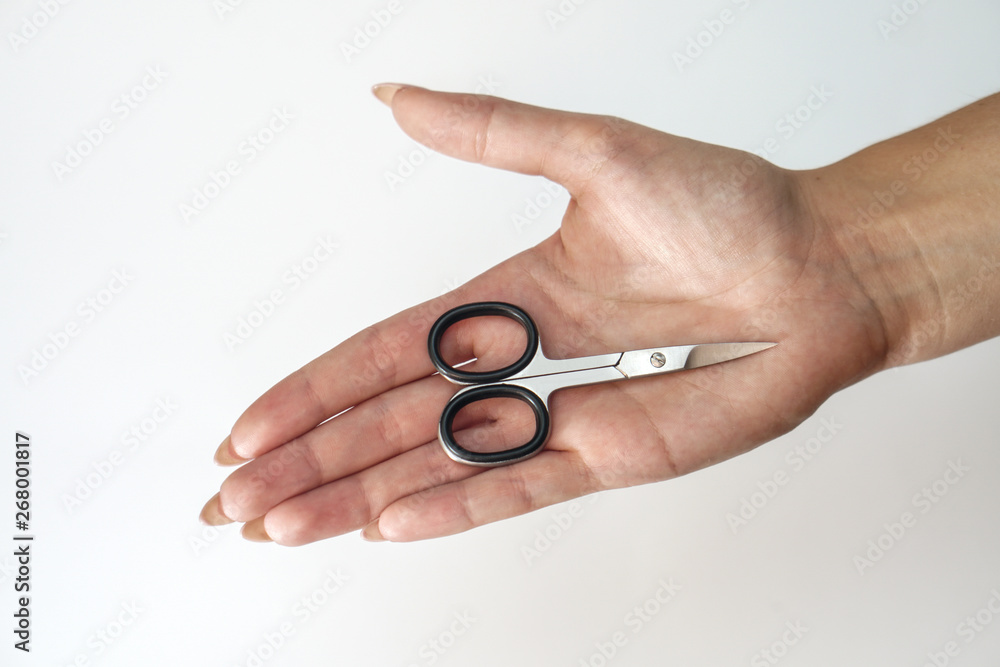 Manicure scissors on the hand of a young girl. Female beauty and body care. Stock photo