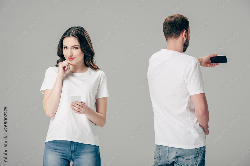 smiling attractive girl in white t-shirt standing near young man taking selfie with smartphone isolated on grey smiling attractive girl in white t-shirt standing near young man taking selfie with smartphone isolated on grey