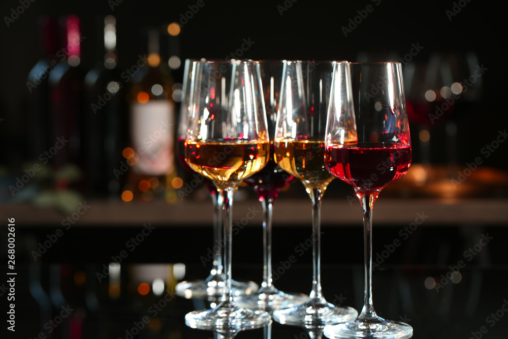 Glasses with different wines on bar counter against blurred background. Space for text